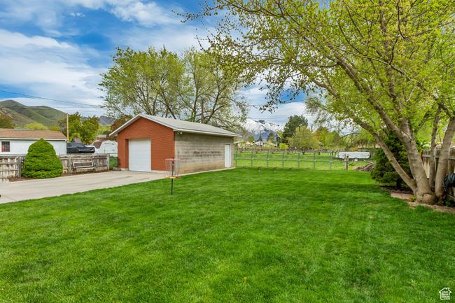 View of yard featuring fence, concrete driveway, an outbuilding, a detached garage, and a mountain view | Image 20