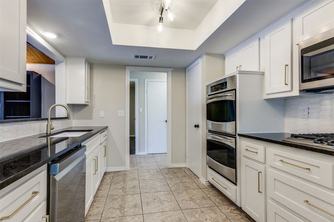 Kitchen with appliances with stainless steel finishes, a raised ceiling, white cabinets, and tasteful backsplash | Image 13