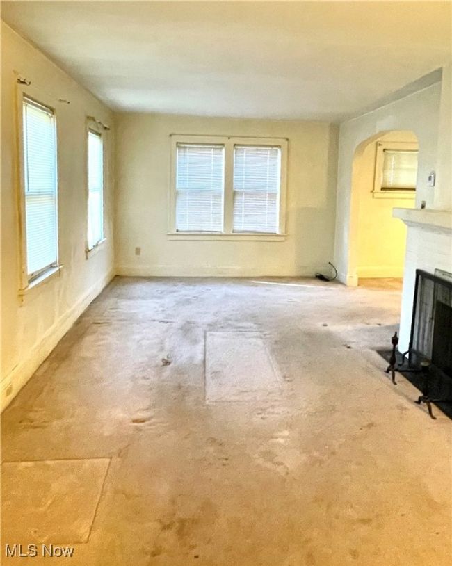 Unfurnished living room featuring arched walkways, a fireplace with flush hearth, carpet, and baseboards | Image 4