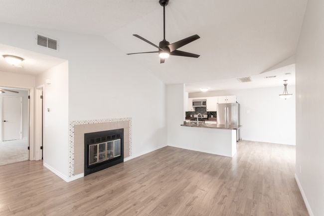 Unfurnished living room with ceiling fan, light wood-style floors, high vaulted ceiling, and a tile fireplace | Image 6