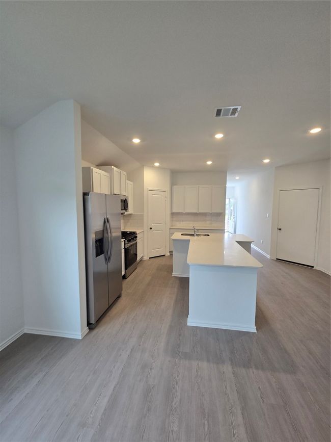 Kitchen with refrigerator, stove, recessed lighting, white cabinets, and a kitchen island with sink | Image 10