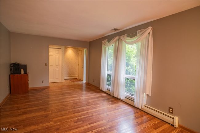 Empty room featuring wood finished floors, a baseboard radiator, and baseboards | Image 21