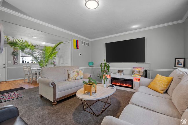 Living room with ornamental molding, a warm lit fireplace, and wood finished floors | Image 4