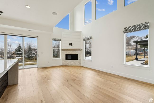 Living room featuring a glass covered fireplace, light wood-type flooring, baseboards, and a towering ceiling | Image 15
