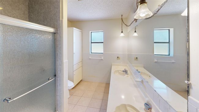 Bathroom with tile walls, tile patterned floors, plenty of natural light, double vanity, and a stall shower | Image 9