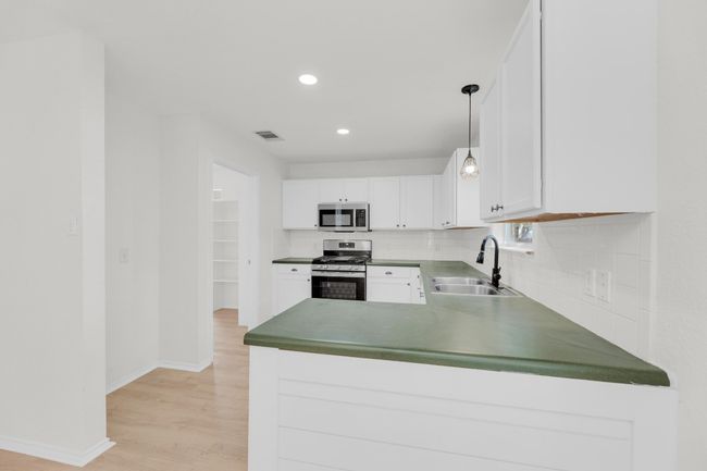 Kitchen featuring light wood finished floors, stainless steel appliances, a sink, baseboards, and decorative backsplash | Image 8