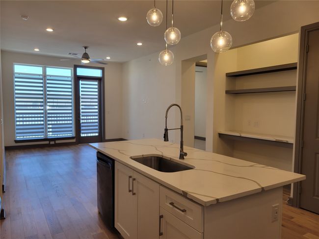 Kitchen featuring a sink, a center island with sink, black dishwasher, wood finished floors, and open shelves | Image 7