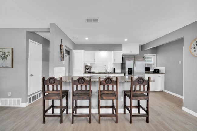 Kitchen featuring white cabinets, a breakfast bar area, stainless steel refrigerator with ice dispenser, and visible vents | Image 8