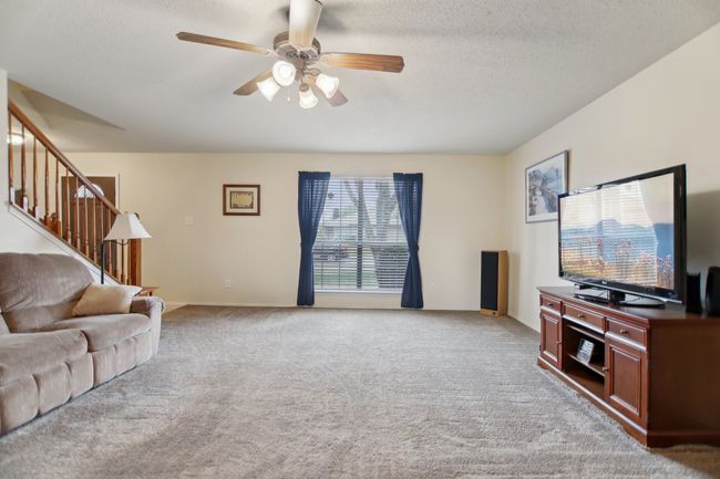 Living area featuring carpet floors, stairway, a textured ceiling, baseboards, and ceiling fan | Image 4