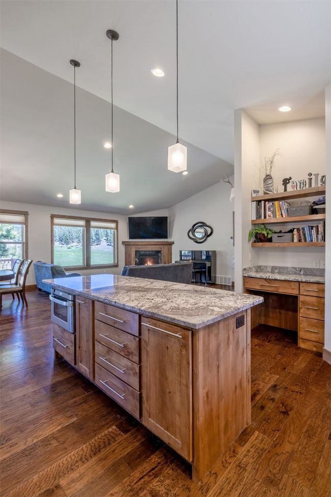 Kitchen with open floor plan, dark wood-style floors, a kitchen island, lofted ceiling, and light stone countertops | Image 12