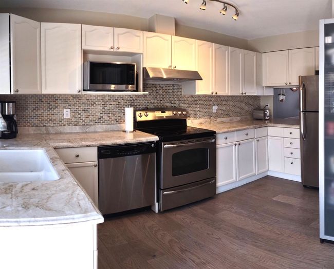 Kitchen featuring white cabinets, dark wood-style flooring, under cabinet range hood, and stainless steel appliances | Image 6