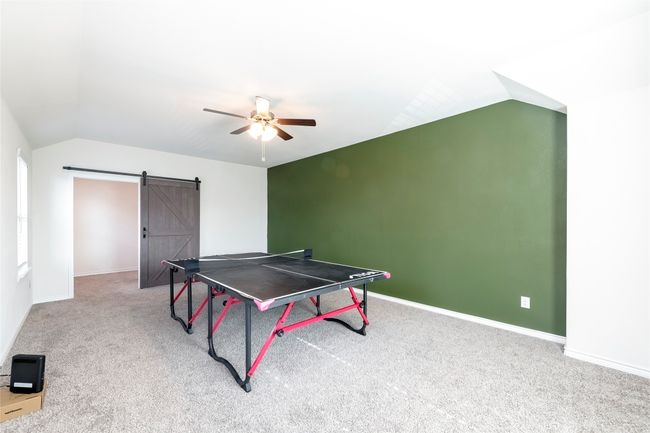 Recreation room featuring a barn door, light carpet, lofted ceiling, and a ceiling fan | Image 21