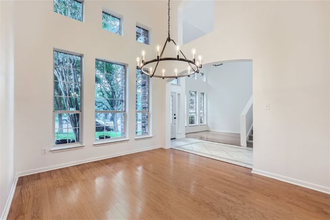 Unfurnished dining area featuring a chandelier, a towering ceiling, hardwood / wood-style flooring, baseboards, and stairway | Image 6