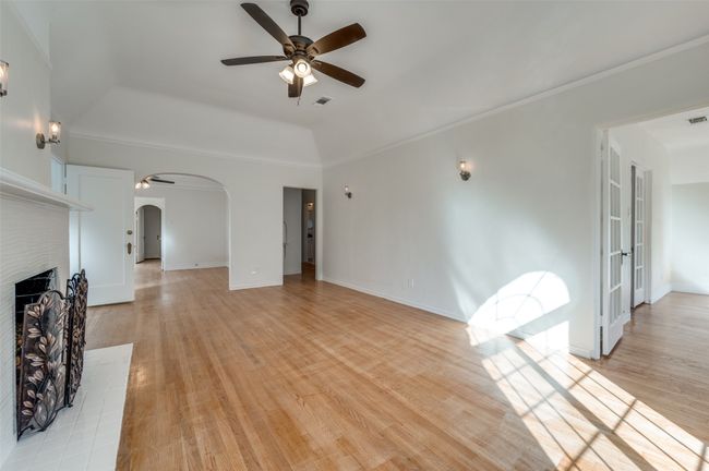 Unfurnished living room with arched walkways, ceiling fan, a raised ceiling, light wood-type flooring, and a fireplace | Image 22