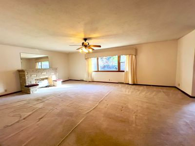 Unfurnished living room featuring a stone fireplace, light colored carpet, and ceiling fan | Image 3