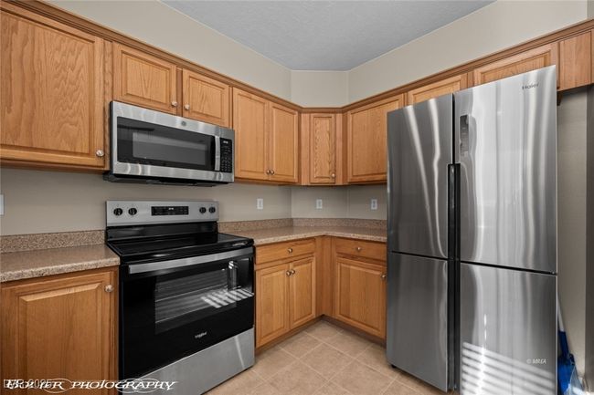 Kitchen with light tile patterned flooring, light countertops, stainless steel appliances, and brown cabinetry | Image 12