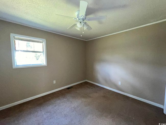 Carpeted empty room featuring a ceiling fan, crown molding, baseboards, and a textured ceiling | Image 11