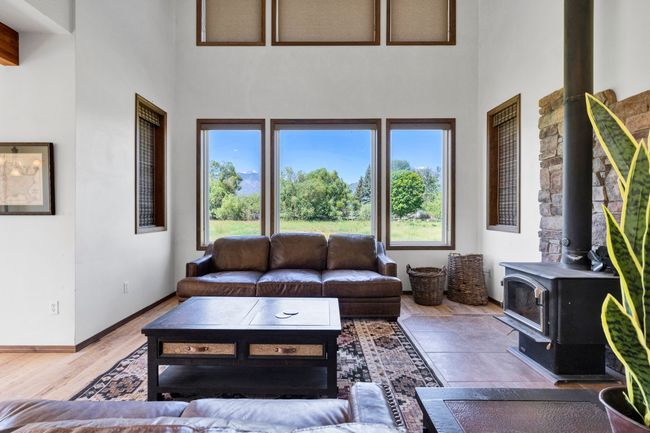 Living area with a towering ceiling, healthy amount of natural light, a wood stove, baseboards, and wood finished floors | Image 15