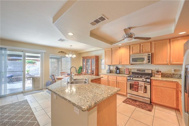 Kitchen featuring stainless steel appliances, a tray ceiling, light brown cabinets, recessed lighting, and an island with sink | Image 27