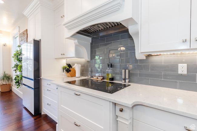 Kitchen with black electric cooktop, custom range hood, freestanding refrigerator, and decorative backsplash | Image 12
