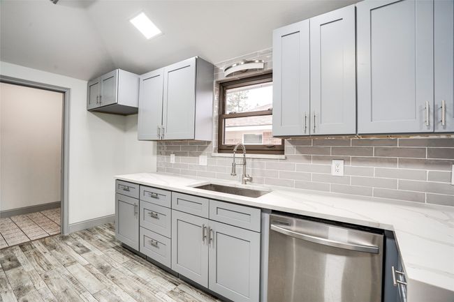 Kitchen featuring stainless steel dishwasher, a sink, lofted ceiling, tasteful backsplash, and light stone counters | Image 7