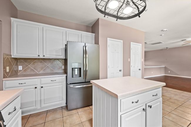 Kitchen with stainless steel fridge with ice dispenser, light tile patterned flooring, decorative backsplash, open floor plan, and light countertops | Image 14
