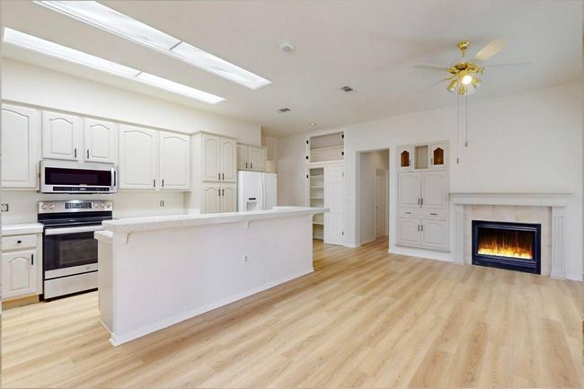 Kitchen featuring stainless steel range with electric stovetop, light wood-style flooring, a fireplace, white fridge with ice dispenser, and light countertops | Image 14