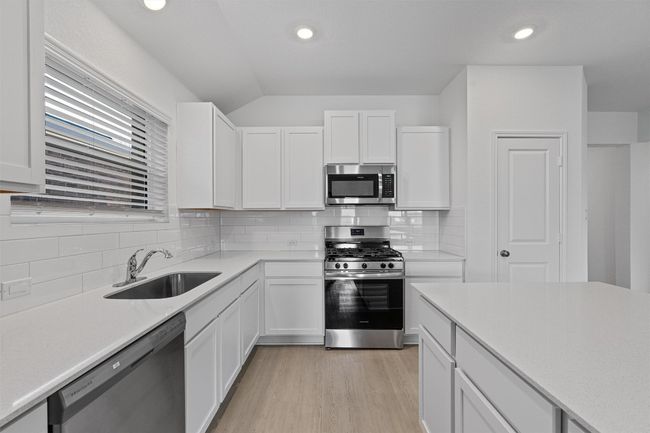 Kitchen featuring stainless steel appliances, light countertops, white cabinets, light wood-style flooring, and vaulted ceiling | Image 5