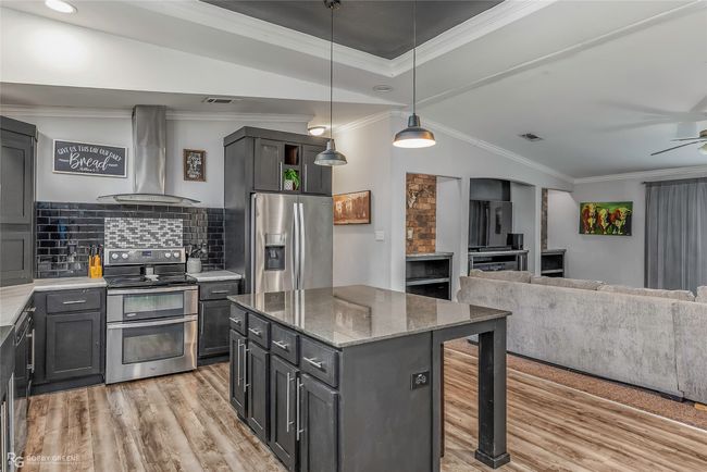 Kitchen featuring tasteful backsplash, light wood-style floors, appliances with stainless steel finishes, wall chimney exhaust hood, and crown molding | Image 22