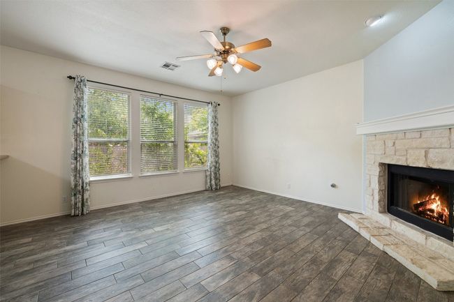 Unfurnished living room featuring ceiling fan, visible vents, a fireplace, baseboards, and dark wood-type flooring | Image 22