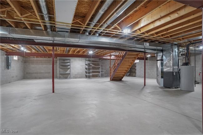 Unfinished below grade area with electric panel, heating unit, water heater, and stairs | Image 41