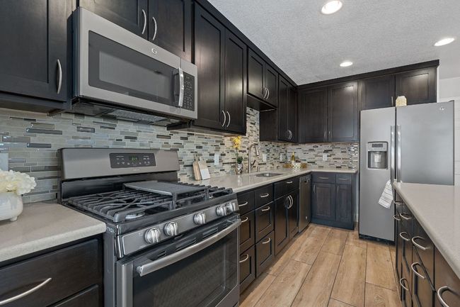 Kitchen featuring appliances with stainless steel finishes, light countertops, light wood-style flooring, tasteful backsplash, and a textured ceiling | Image 24