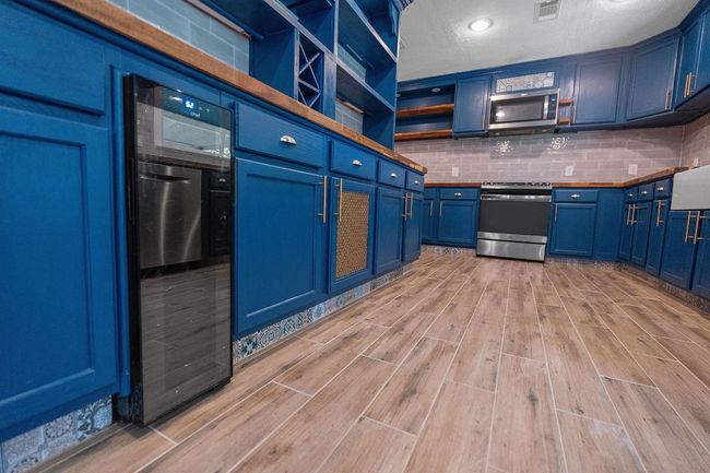 Kitchen with stainless steel appliances, blue cabinetry, light wood-style floors, decorative backsplash, and open shelves | Image 16