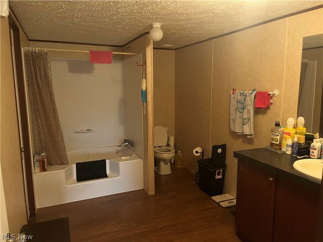 Full bathroom featuring a textured ceiling, hardwood / wood-style floors, shower / bath combo, toilet, and vanity | Image 10