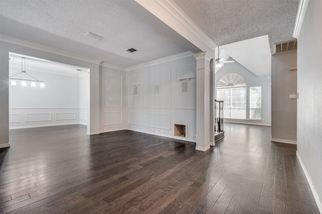 Unfurnished living room with dark wood finished floors, a decorative wall, crown molding, and visible vents | Image 5