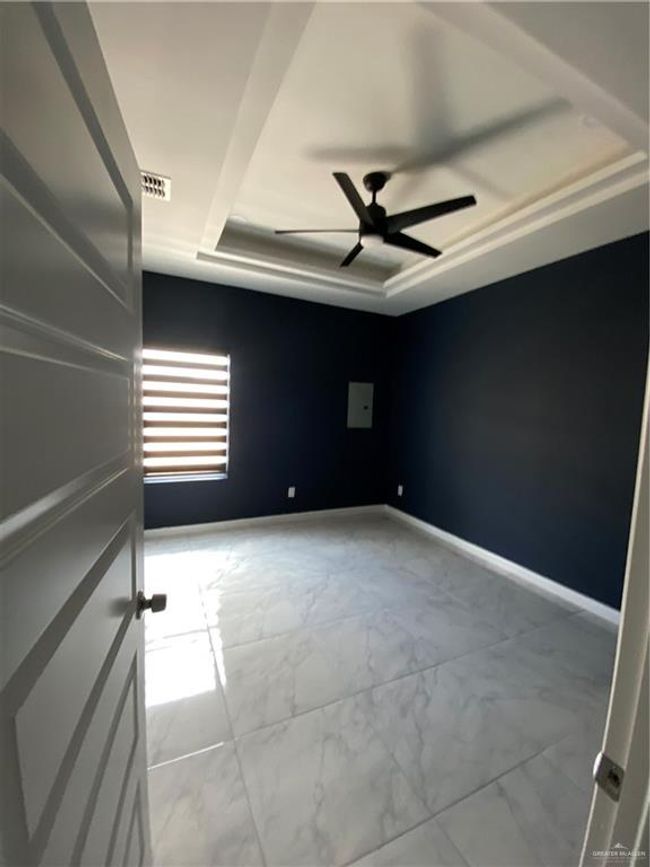 Empty room featuring a tray ceiling, marble look tile flooring, and a ceiling fan | Image 13