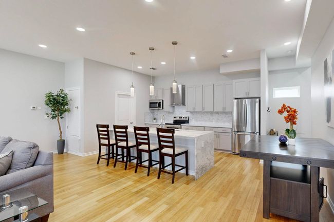 Kitchen featuring stainless steel appliances, wall chimney exhaust hood, a kitchen bar, tasteful backsplash, and light wood finished floors | Image 6