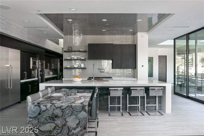Kitchen with decorative backsplash, a breakfast bar, light countertops, built in appliances, and modern cabinets | Image 19