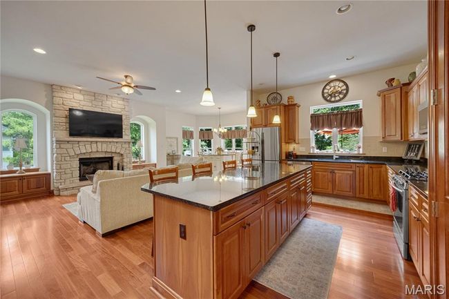 Kitchen featuring appliances with stainless steel finishes, open floor plan, ceiling fan, light wood-style floors, and a fireplace | Image 18