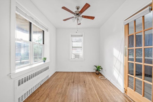 Empty room featuring radiator heating unit, plenty of natural light, wood finished floors, and ceiling fan | Image 8