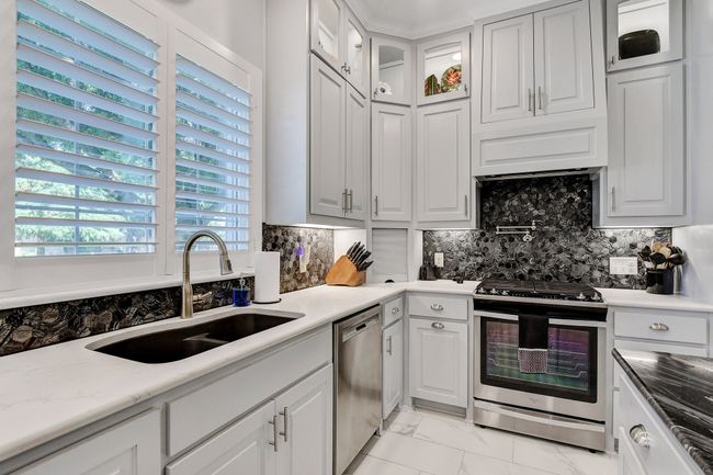 Kitchen with stainless steel appliances, light marble finish flooring, tasteful backsplash, and white cabinets | Image 14