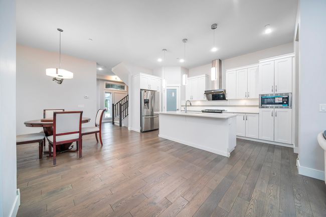 Kitchen with stainless steel appliances, wall chimney range hood, wood finished floors, light countertops, and an island with sink | Image 10