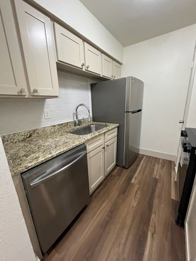 Kitchen with stainless steel appliances, a sink, dark wood finished floors, backsplash, and light stone counters | Image 4