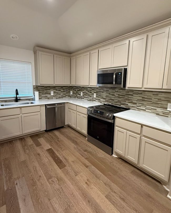 Kitchen with stainless steel appliances, light wood-style floors, light countertops, and backsplash | Image 8
