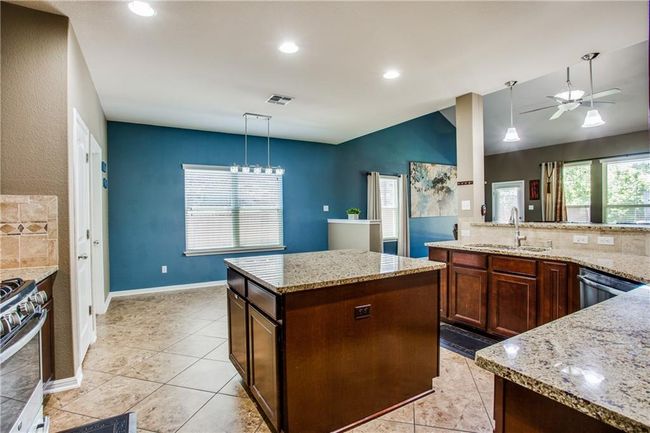 Kitchen with stainless steel appliances, a ceiling fan, light stone counters, hanging light fixtures, and recessed lighting | Image 9