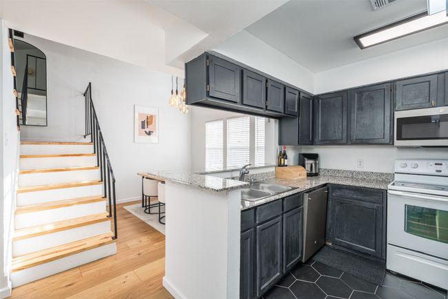 Kitchen featuring appliances with stainless steel finishes, a sink, a peninsula, dark wood-style floors, and light stone countertops | Image 9