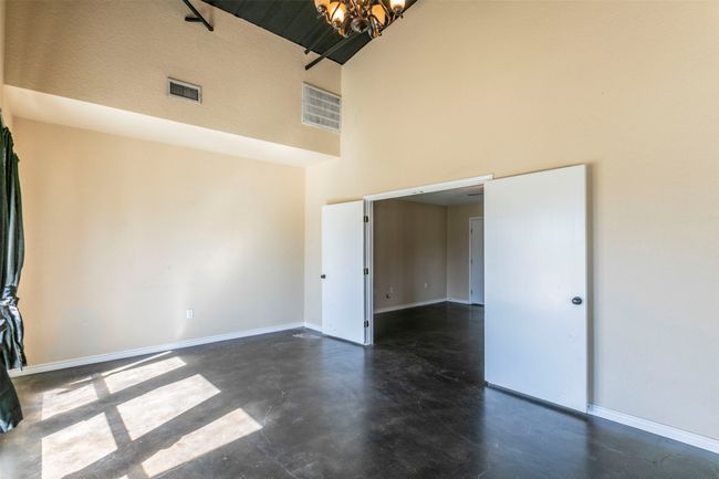 Unfurnished room featuring finished concrete flooring, visible vents, a towering ceiling, an inviting chandelier, and baseboards | Image 12