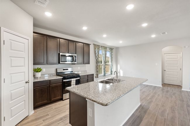 Kitchen featuring a sink, stainless steel appliances, wood tiled floor, visible vents, and dark brown cabinets | Image 23