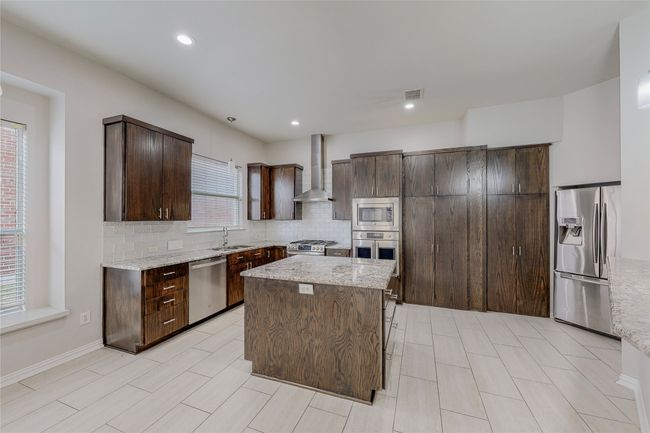 Kitchen with stainless steel appliances, wall chimney exhaust hood, a sink, dark brown cabinets, and decorative backsplash | Image 16