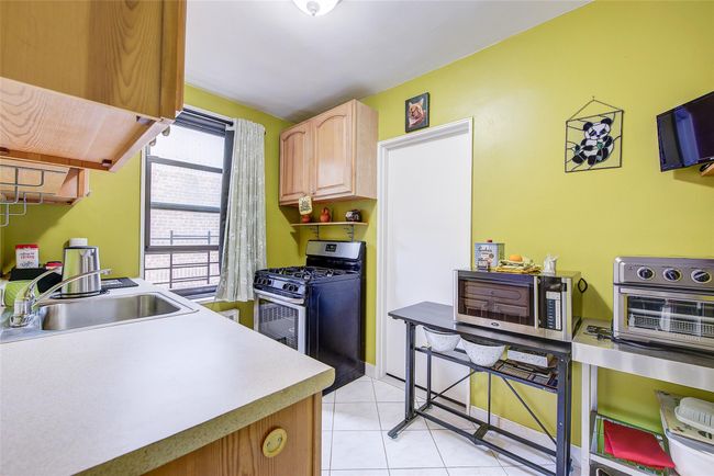 Kitchen featuring stainless steel appliances, light tile patterned flooring, light countertops, ventilation hood, and light brown cabinets | Image 11